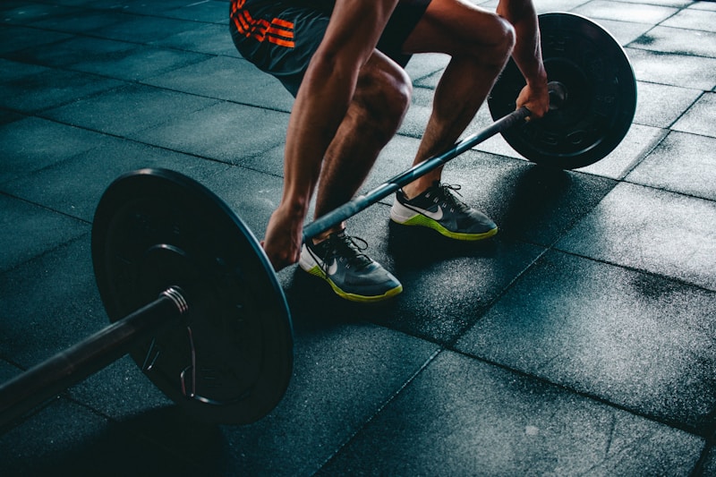 Person in a crouched deadlift starting position gripping a loaded barbell on rubber gym flooring